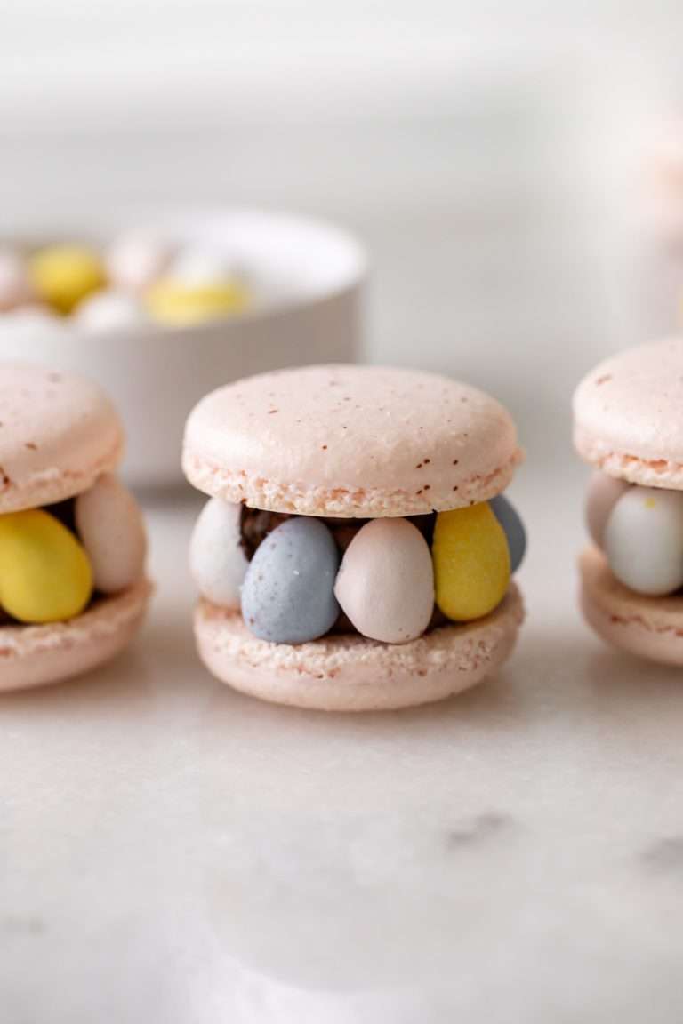 Festive Cadbury Mini Egg macarons for Easter and spring, featuring speckled shells, chocolate buttercream and halved Cadbury mini egg candies. They are chocolaty, delicious and an adorable treat for the for the season! Inspired by the Ispahan Macaron. Gluten free recipe.