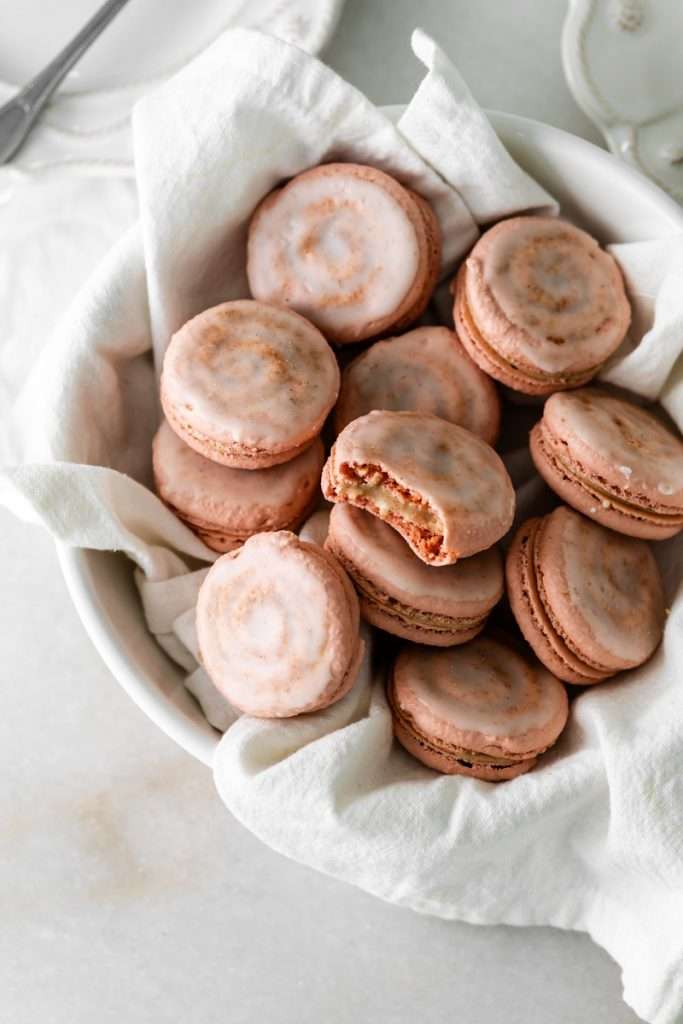 Cinnamon roll flavored macarons for breakfast and brunch. The swirled shells are filled with cinnamon roll white chocolate ganache and topped with icing for the ultimate cinnamon roll flavor. A gluten free recipe.