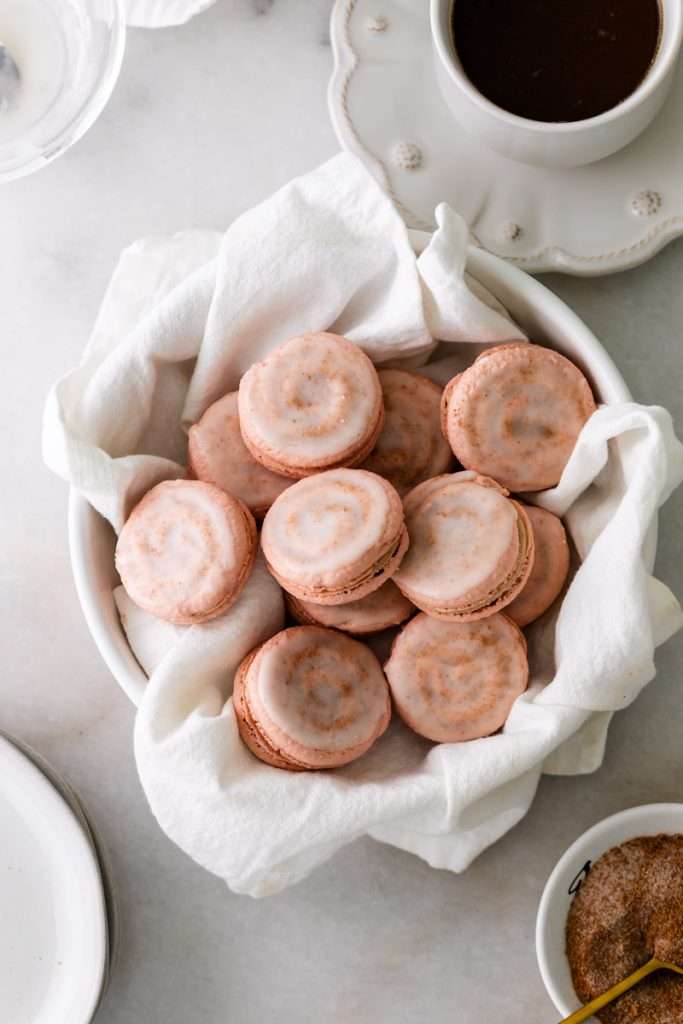 Cinnamon roll flavored macarons for breakfast and brunch. The swirled shells are filled with cinnamon roll white chocolate ganache and topped with icing for the ultimate cinnamon roll flavor. A gluten free recipe.
