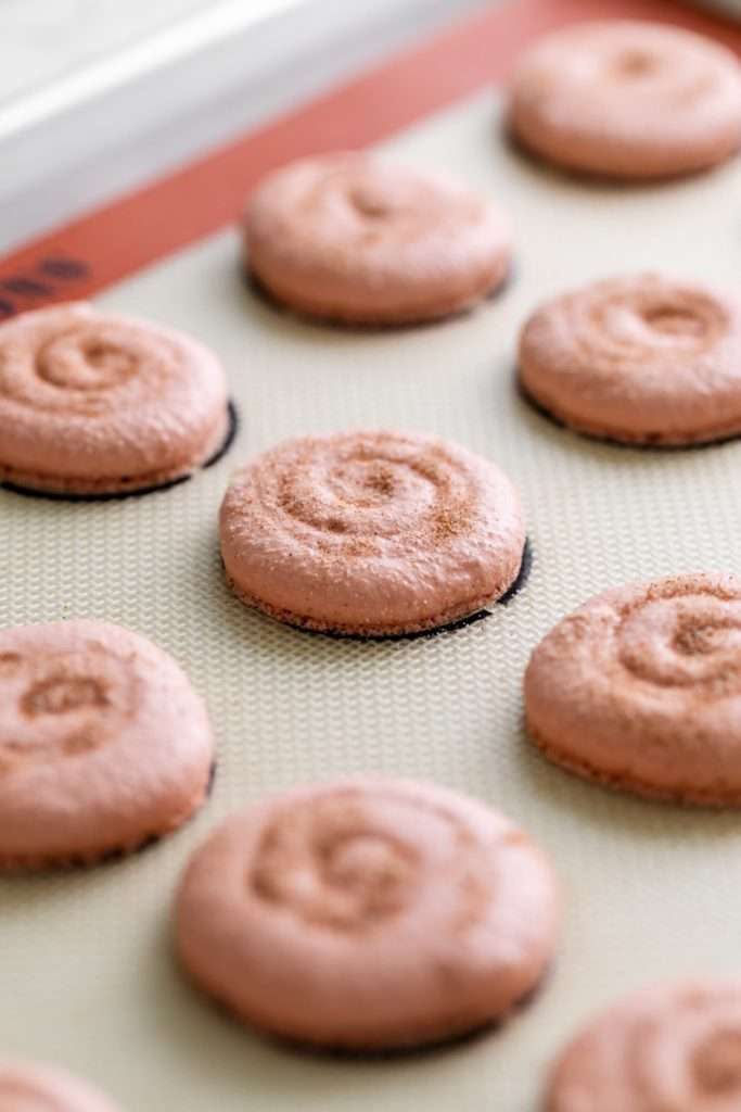 Cinnamon roll flavored macarons for breakfast and brunch. The swirled shells are filled with cinnamon roll white chocolate ganache and topped with icing for the ultimate cinnamon roll flavor. A gluten free recipe.