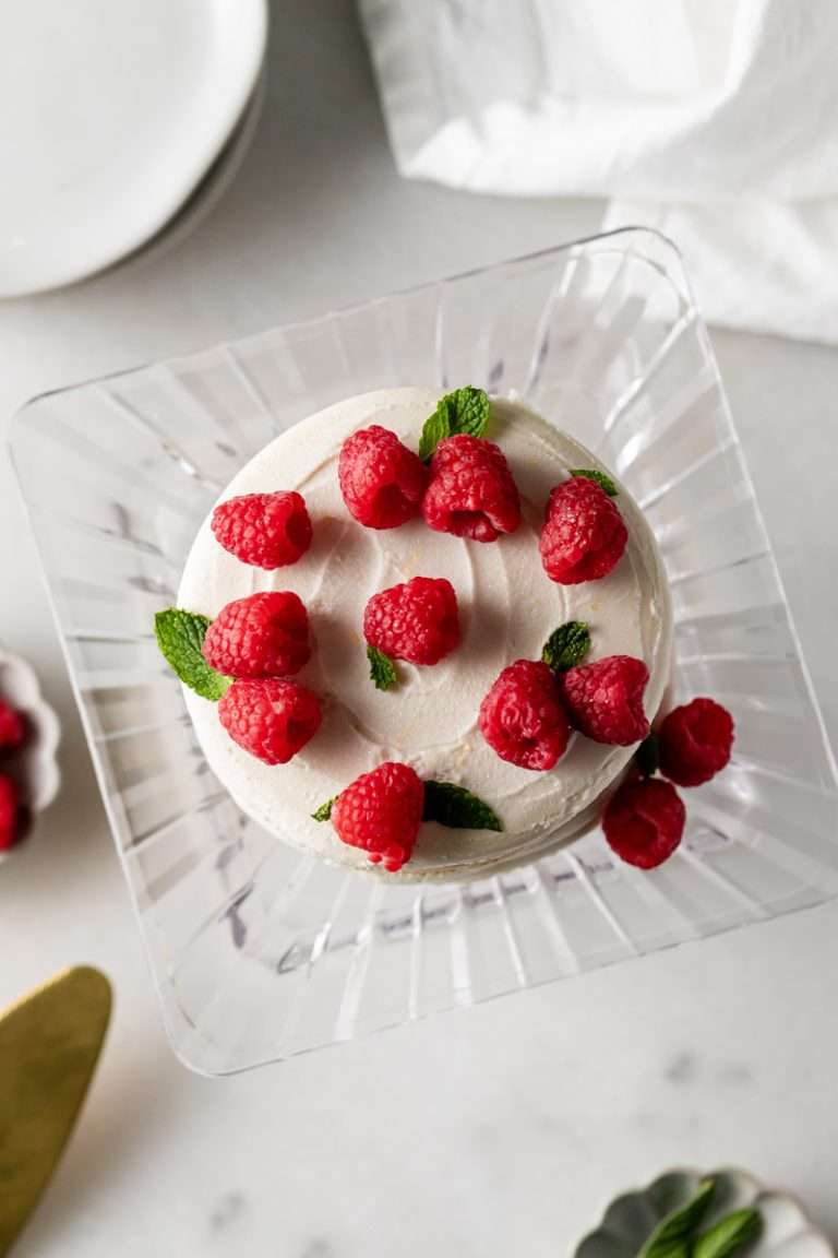 Honey Lemon Macaron cake inspired by With Love, Meghan's honey lemon cake. Layered with four 5" macaron shells, honey lemon frosting, raspberry preserves and topped with clusters of fresh raspberries a mint. A gorgeous and delicious macaron recipe for spring parties and entertaining. Gluten Free with Dairy Free option.