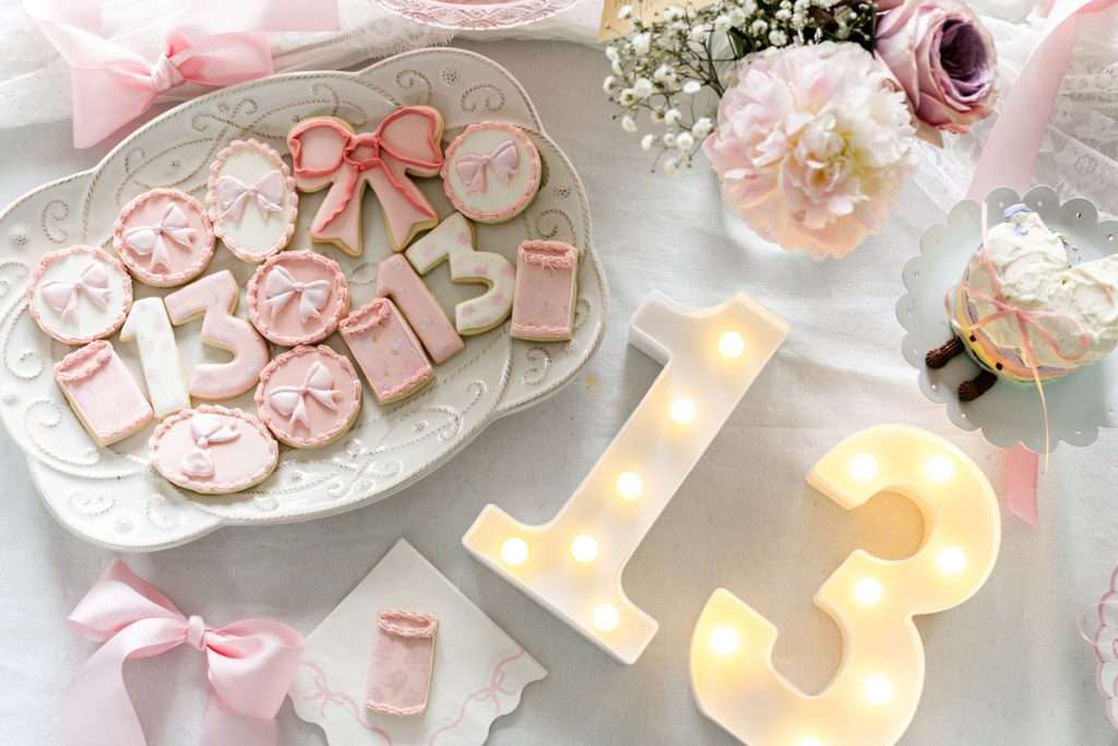Pink party desserts for teen coquette bow themed birthday party, complete with homemade cake and custom sugar cookies.
