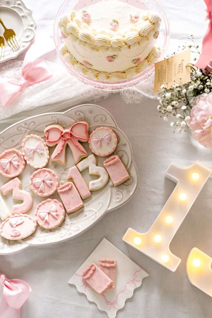Pink party desserts for teen coquette bow themed birthday party, complete with homemade cake and custom sugar cookies.