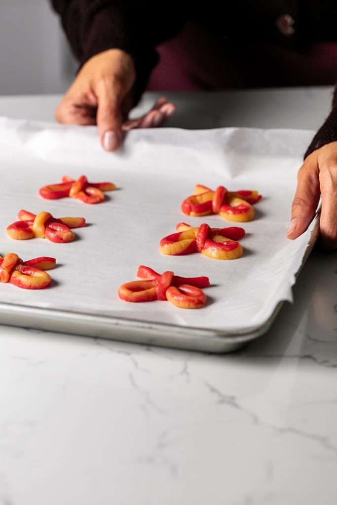 Peppermint infused candy cane bow sugar cookies shaped and twisted into bows and arranged on a holiday themed surface.