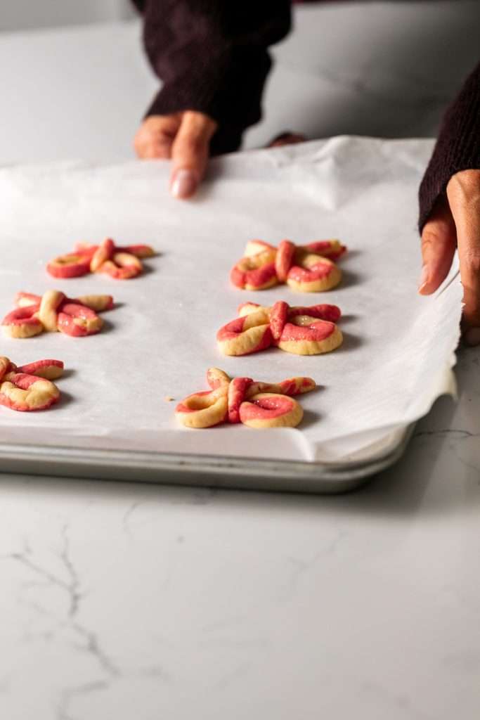 Peppermint infused candy cane bow sugar cookies shaped and twisted into bows and arranged on a holiday themed surface.