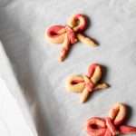 Peppermint infused candy cane bow sugar cookies shaped and twisted into bows and arranged on a holiday themed surface.