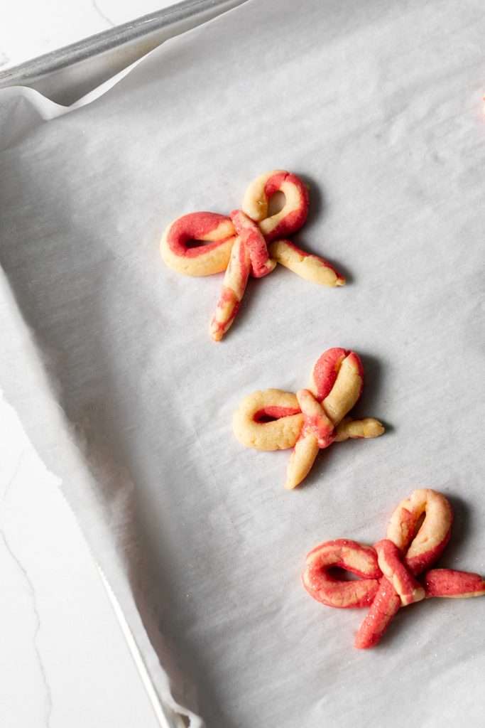 Peppermint infused candy cane bow sugar cookies shaped and twisted into bows and arranged on a holiday themed surface.
