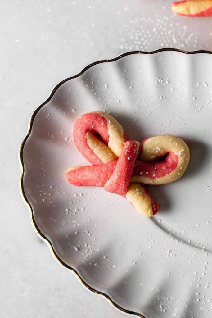 Peppermint infused candy cane bow sugar cookies shaped and twisted into bows and arranged on a holiday themed surface.