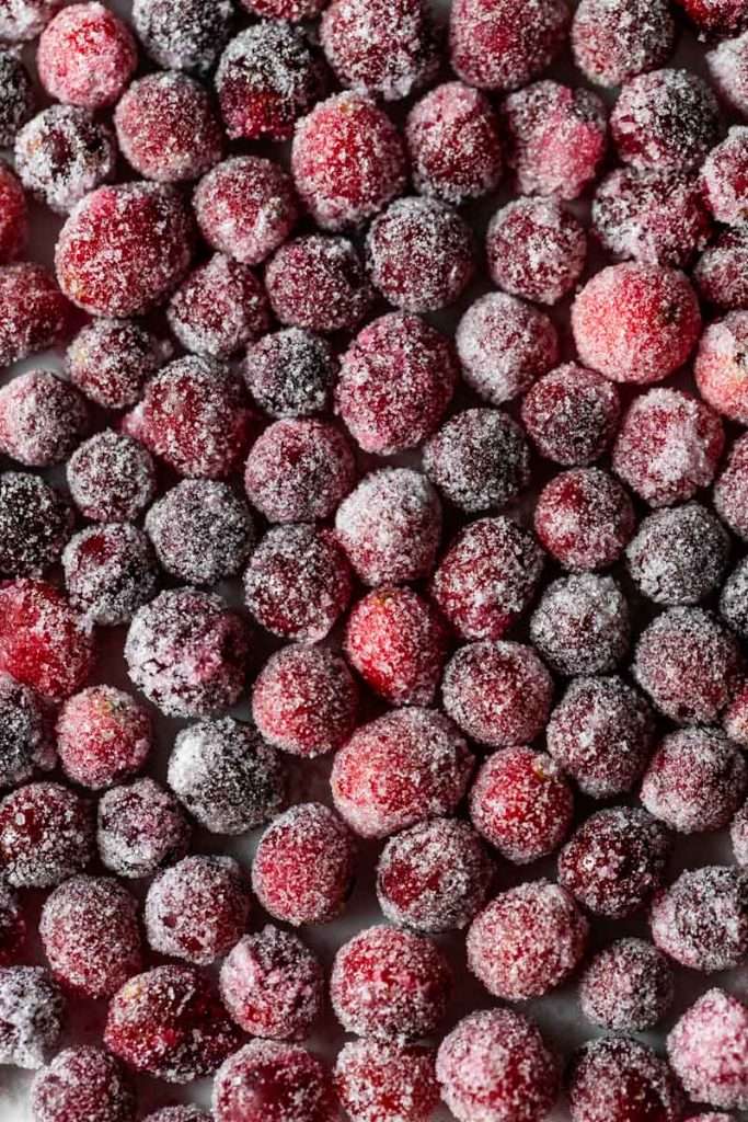 Sparkling sugared cranberries coated in sugar in a glass dish, perfect as a festive holiday garnish.