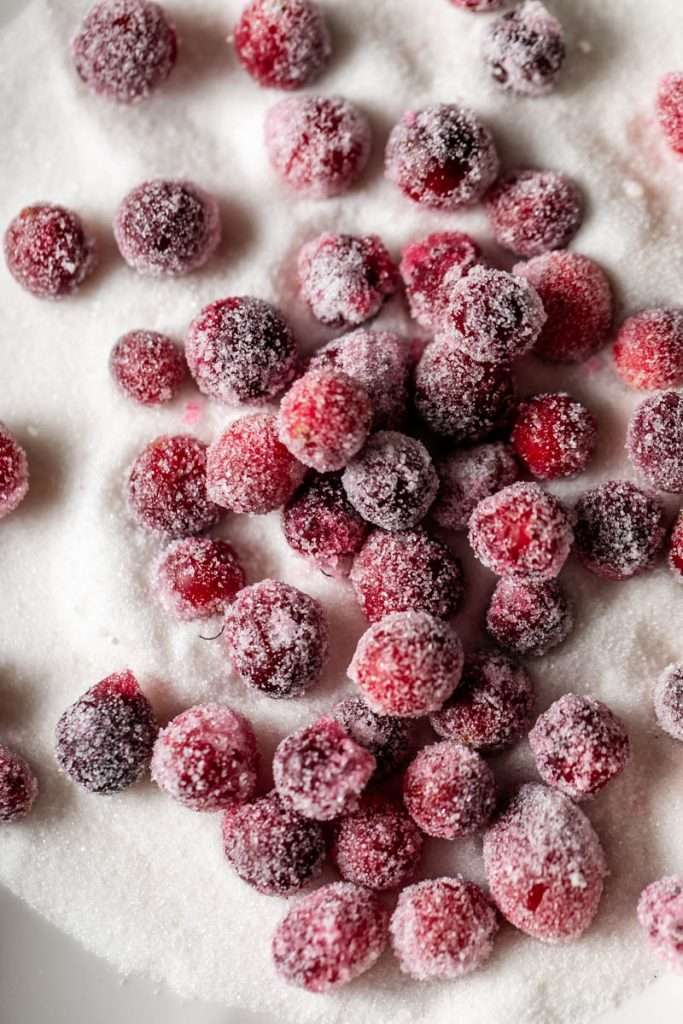 Sparkling sugared cranberries coated in sugar in a glass dish, perfect as a festive holiday garnish.