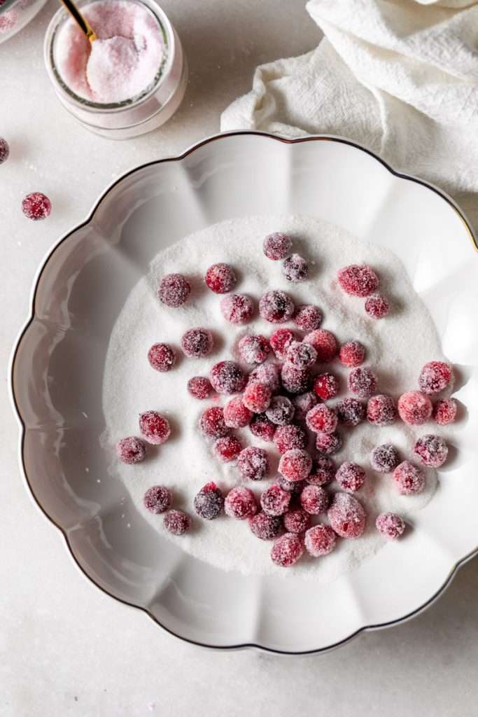 Sparkling sugared cranberries coated in sugar in a glass dish, perfect as a festive holiday garnish.