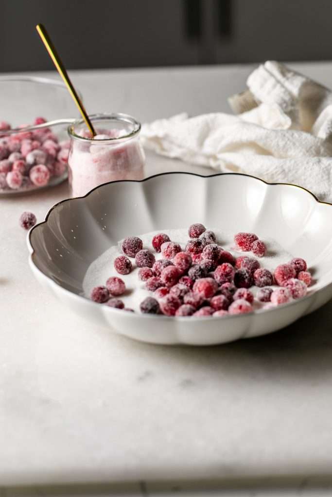 Sparkling sugared cranberries coated in sugar in a glass dish, perfect as a festive holiday garnish.