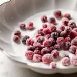 Sparkling sugared cranberries coated in sugar in a glass dish, perfect as a festive holiday garnish.