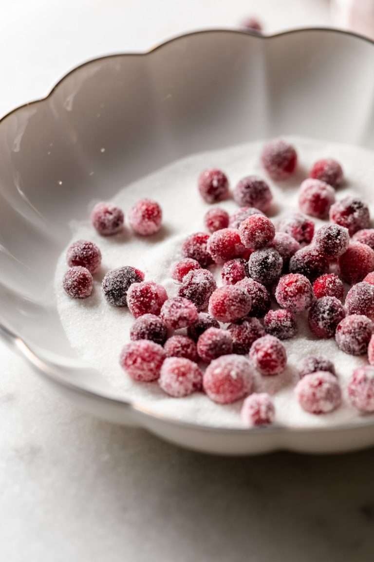 Sparkling sugared cranberries coated in sugar in a glass dish, perfect as a festive holiday garnish.
