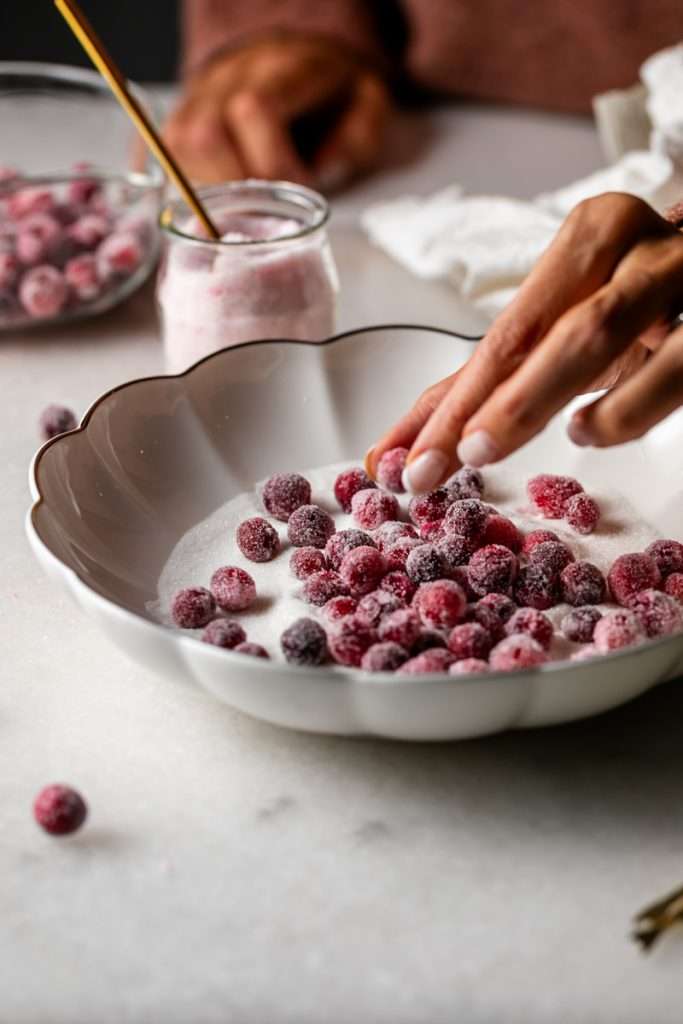 Sparkling sugared cranberries coated in sugar in a glass dish, perfect as a festive holiday garnish.