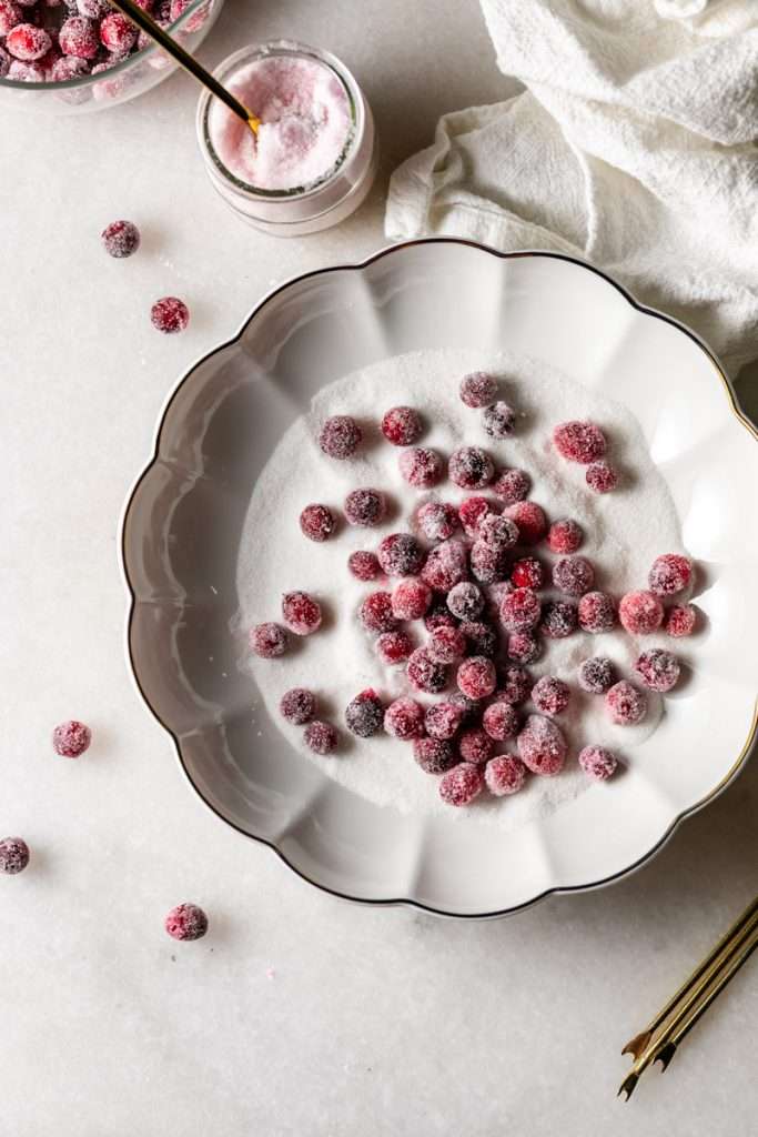 Sparkling sugared cranberries coated in sugar in a glass dish, perfect as a festive holiday garnish.