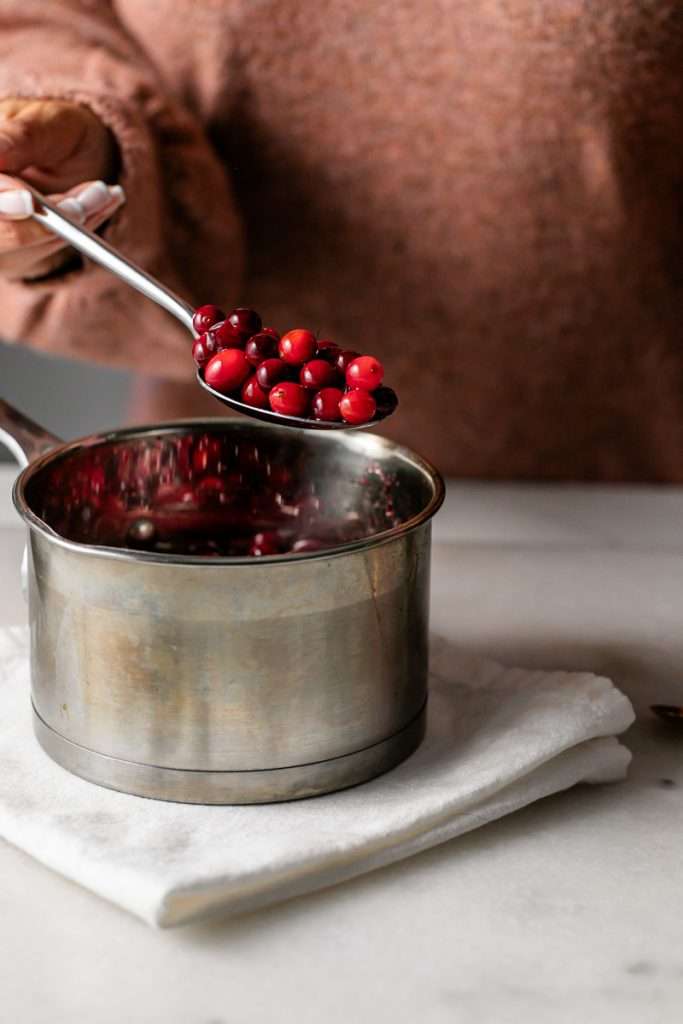 Sparkling sugared cranberries coated in sugar in a glass dish, perfect as a festive holiday garnish.
