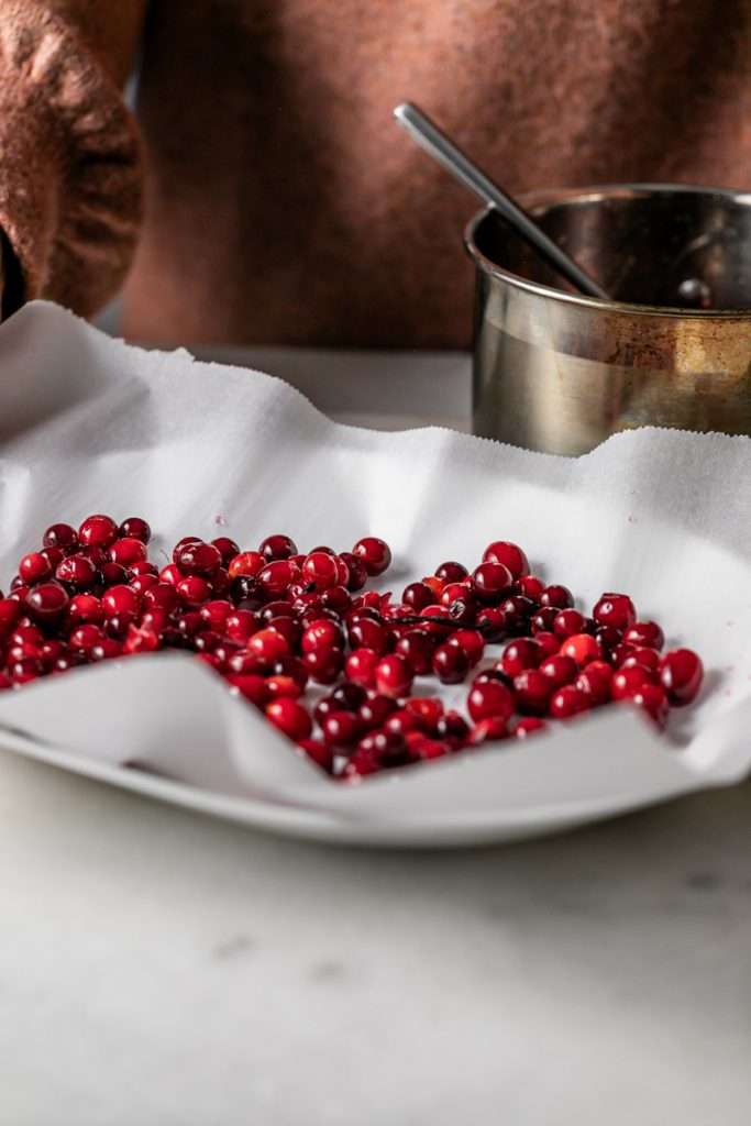 Sparkling sugared cranberries coated in sugar in a glass dish, perfect as a festive holiday garnish.