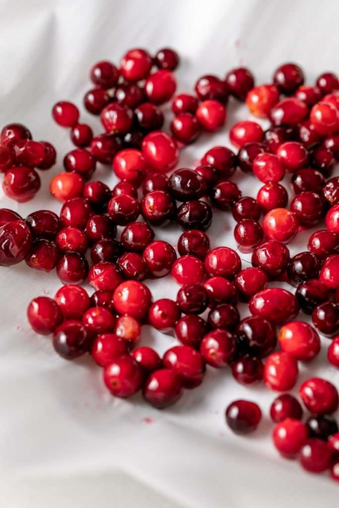 Sparkling sugared cranberries coated in sugar in a glass dish, perfect as a festive holiday garnish.