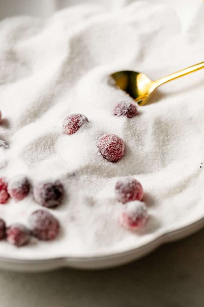 Sparkling sugared cranberries coated in sugar in a glass dish, perfect as a festive holiday garnish.