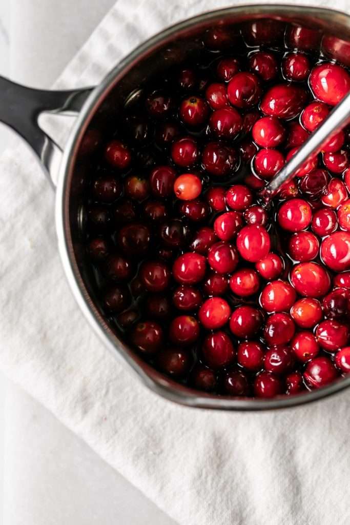 Sparkling sugared cranberries coated in sugar in a glass dish, perfect as a festive holiday garnish.