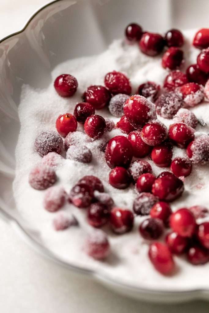 Sparkling sugared cranberries coated in sugar in a glass dish, perfect as a festive holiday garnish.