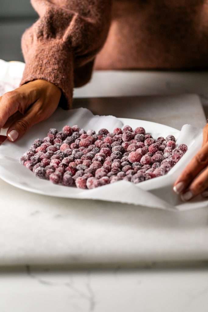 Sparkling sugared cranberries coated in sugar in a glass dish, perfect as a festive holiday garnish.