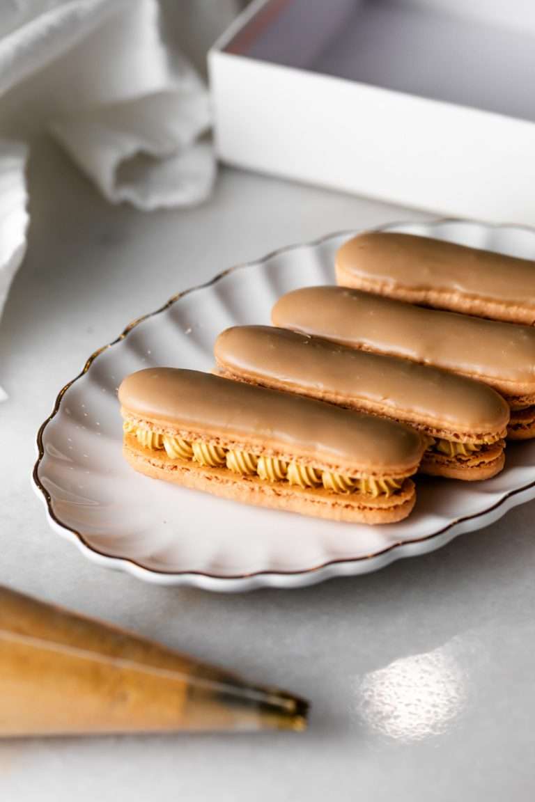 Maple bar macarons with maple buttercream, topped with glossy maple glaze, arranged on a tray. The donut inspired macarons feature a crisp shell and rich maple flavor.