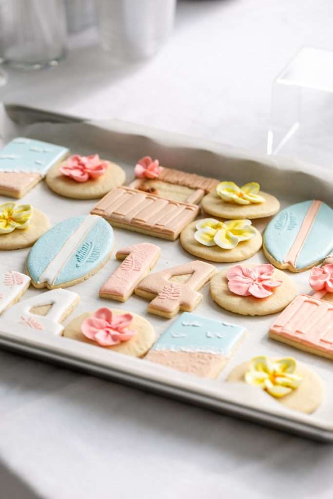 Decorated tropical sugar cookies with royal icing featuring, beaches, surf boards, tropical flowers, tiki huts, and more.