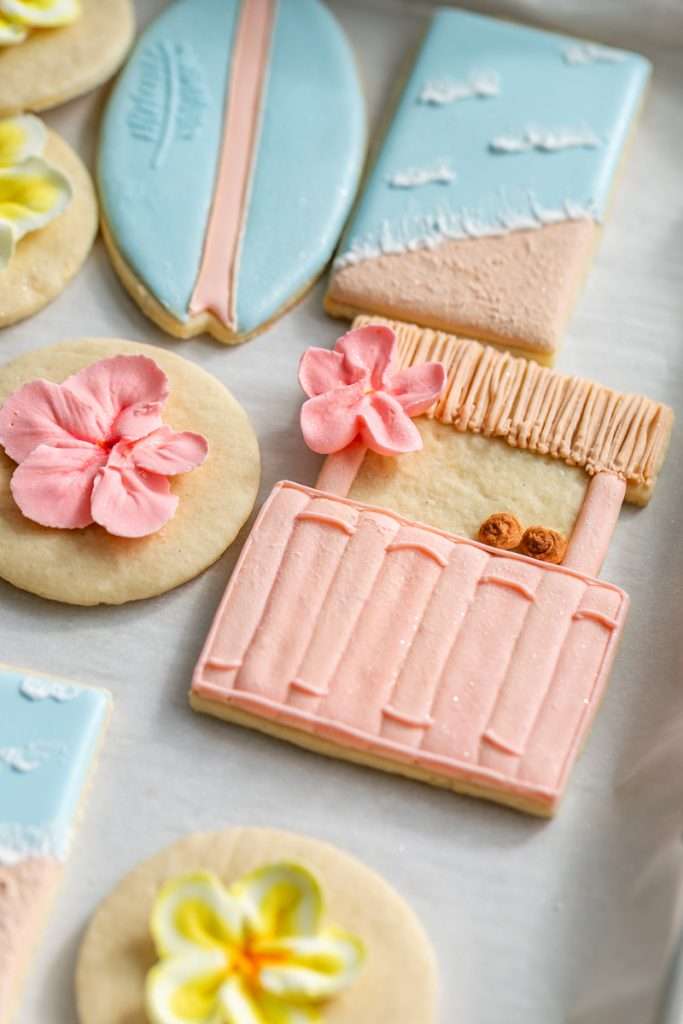 Decorated tropical sugar cookies with royal icing featuring, beaches, surf boards, tropical flowers, tiki huts, and more.