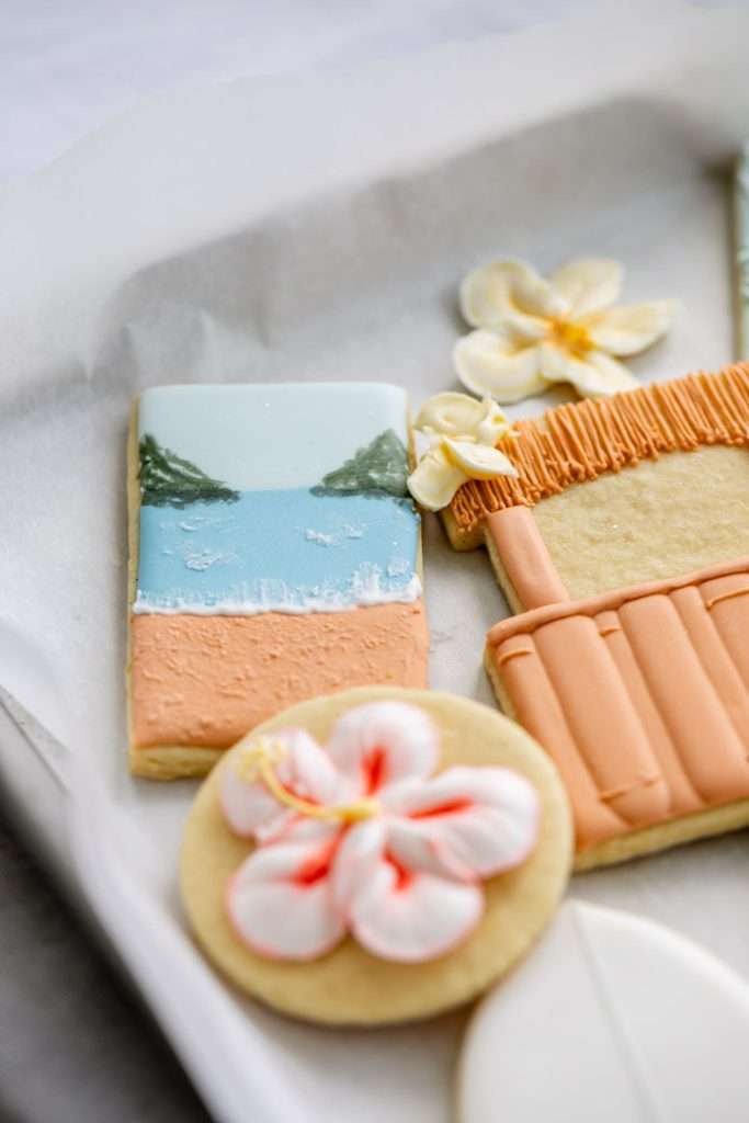 Decorated tropical sugar cookies with royal icing featuring, beaches, surf boards, tropical flowers, tiki huts, and more.