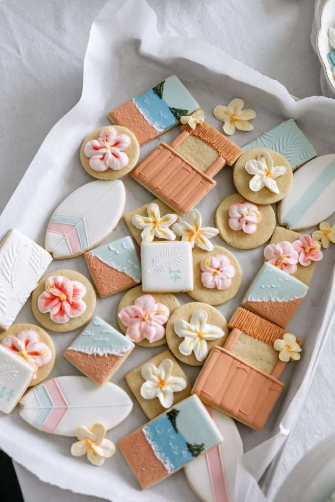 Decorated tropical sugar cookies with royal icing featuring, beaches, surf boards, tropical flowers, tiki huts, and more.