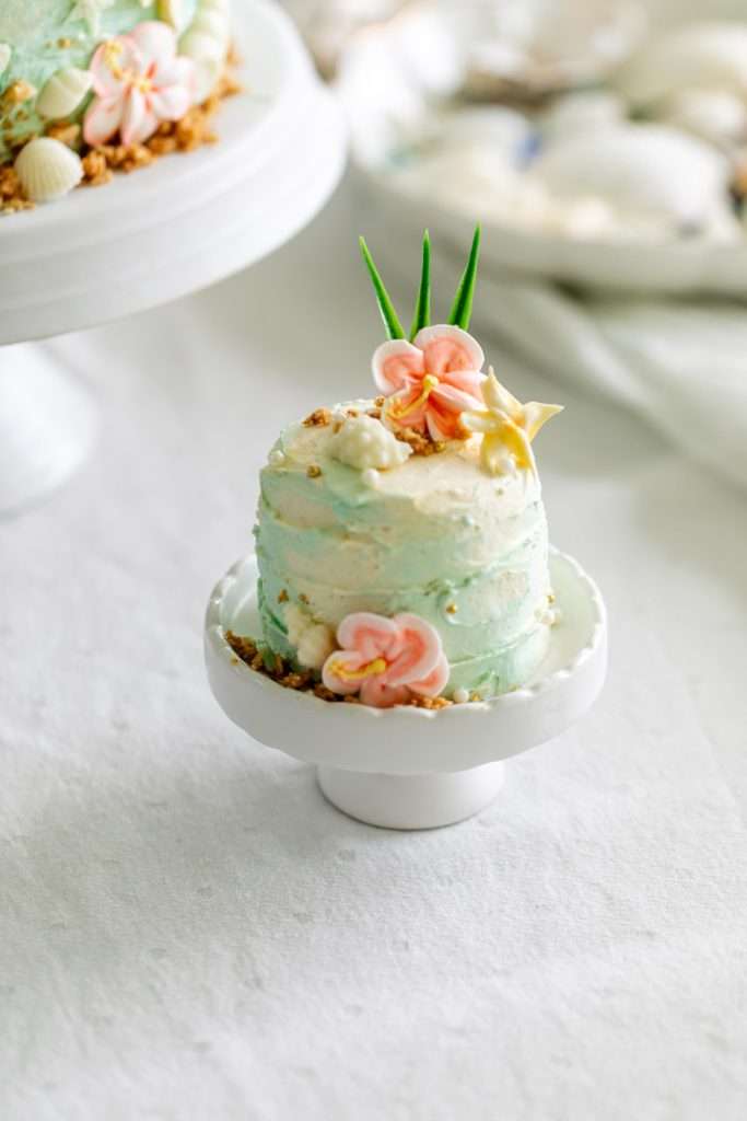 Tropical birthday cake decorated with palm leaves, hibiscus flowers, and beach inspired details.