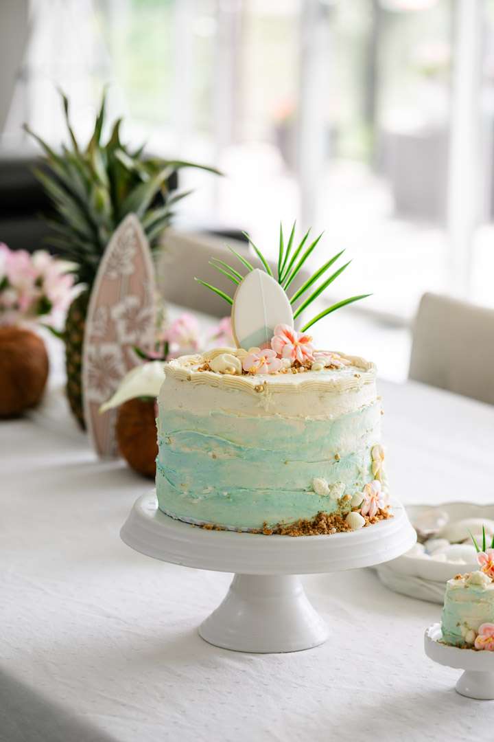 Tropical birthday cake decorated with palm leaves, hibiscus flowers, and beach inspired details.