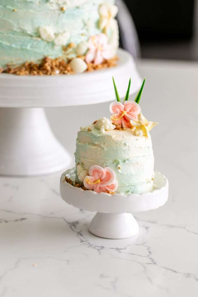 Tropical beach mini birthday cake decorated with palm leaves, hibiscus flowers, and beach inspired details.
