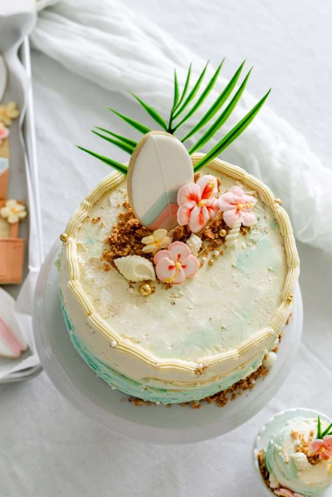 Tropical beach birthday cake decorated with palm leaves, hibiscus flowers, and island inspired details.