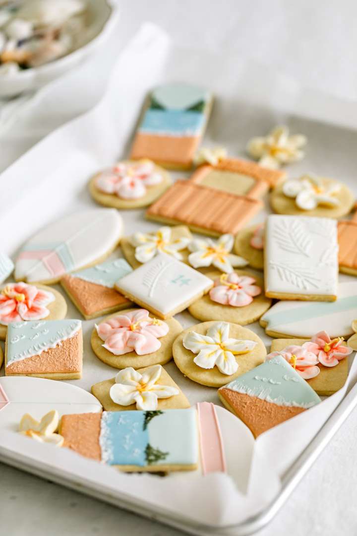 Decorated tropical sugar cookies with royal icing featuring, beaches, surf boards, tropical flowers, tiki huts, and more.