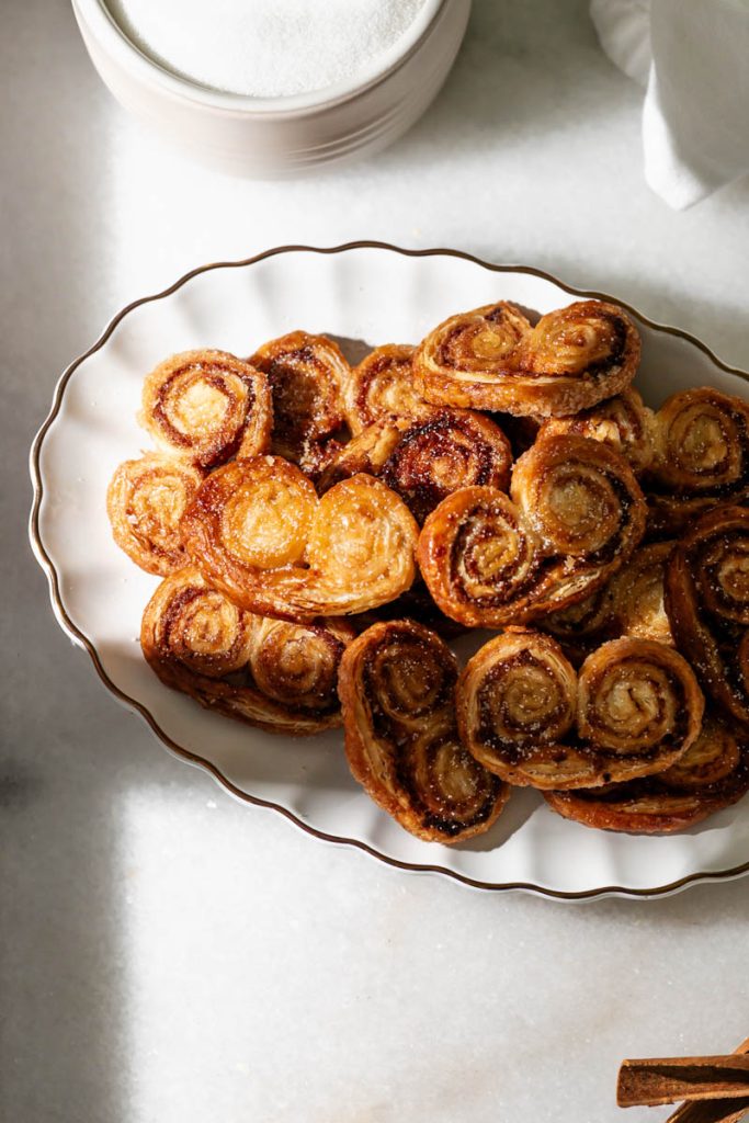 Golden apple cinnamon palmiers made with flaky puff pastry, cinnamon and apple, on a serving plate.