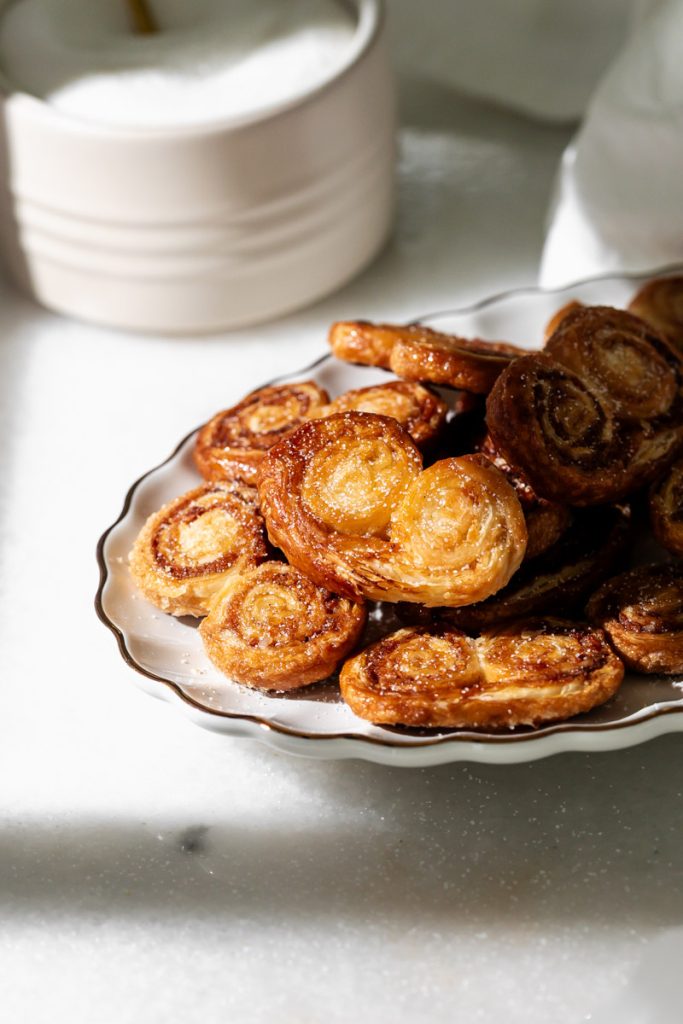 Golden apple cinnamon palmiers made with flaky puff pastry, cinnamon and apple, on a serving plate.