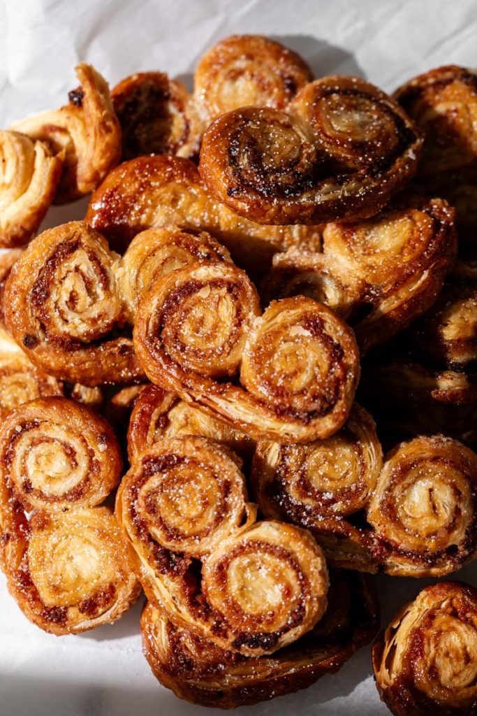 Golden apple cinnamon palmiers made with flaky puff pastry, cinnamon and apple, on a serving plate.