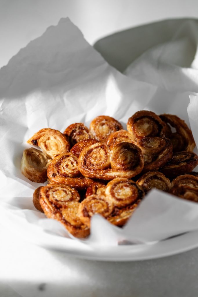 Golden apple cinnamon palmiers made with flaky puff pastry, cinnamon and apple, on a serving plate.