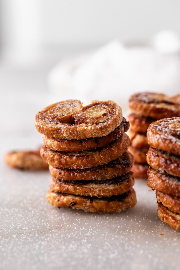 Golden apple cinnamon palmiers made with flaky puff pastry, cinnamon and apple, on a serving plate.