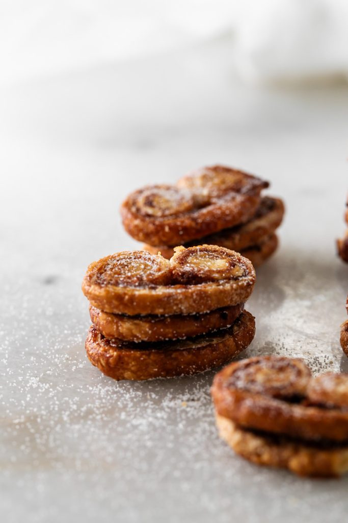Golden apple cinnamon palmiers made with flaky puff pastry, cinnamon and apple, on a serving plate.