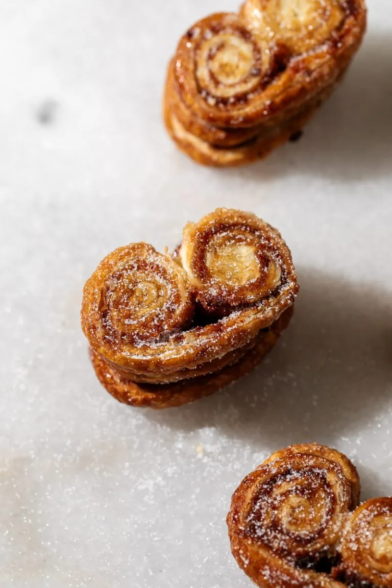 Golden apple cinnamon palmiers made with flaky puff pastry, cinnamon and apple, on a serving plate.