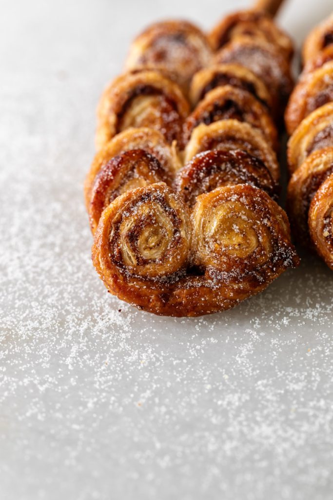 Golden apple cinnamon palmiers made with flaky puff pastry, cinnamon and apple, on a serving plate.
